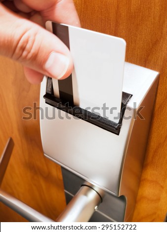 Person\'s hand sliding a keycard into a hotel room electronic door lock to unlock the door