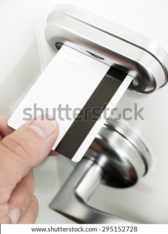 A person\'s hand unlocking a hotel room keycard door lock by inserting a magnetic stripe key card