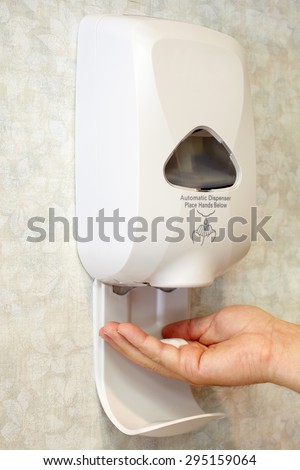Picture of a wall mounted automatic sanitizer dispenser with a male hand and liquid soap.