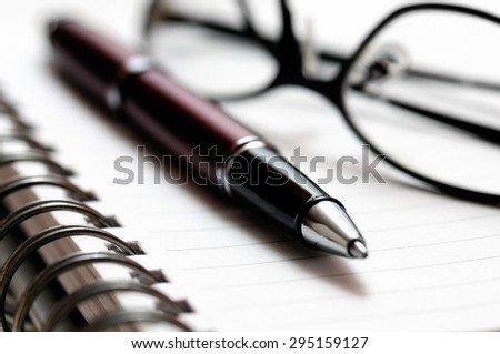 Picture of ballpoint pen and prescription glasses on a spiral notebook