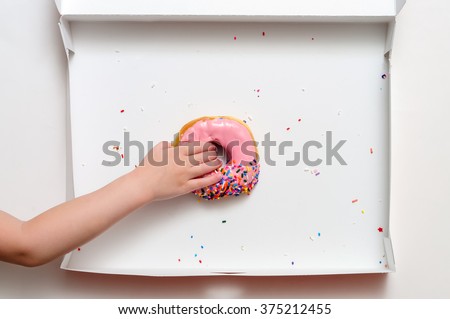 Donut box with a young female child\'s hand reaching to grab the last pink strawberry frosted doughnut