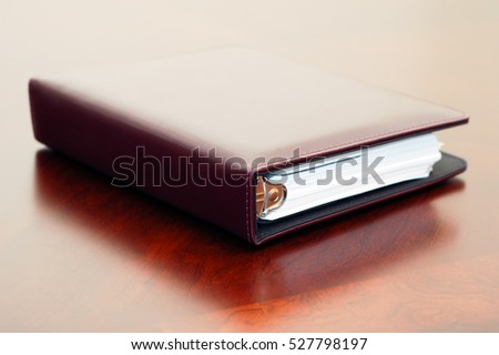 Stock picture of a closed brown day planner on a wooden office desk.