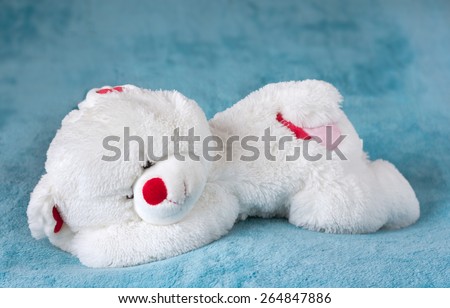 White teddy bear stuffed toy sleeping on a soft blue velvet blanket