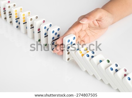 Human hand stopping a line of dominoes from falling. concept image for recovery plan and solution for cascading failures and problems. Dominoes are placed on a white table. High key image .