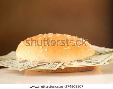 Concept image for rich and greedy. US dollar bills stuffed between burger buns. Burger is placed on a white desk with a brown vignetted background.