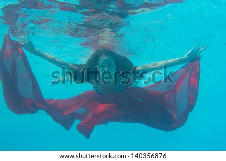 woman submerged with red fabric under water
