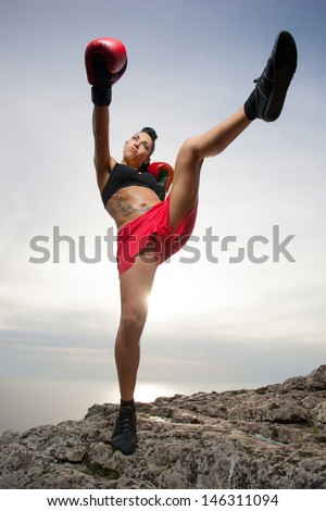 Beautiful kick boxing girl exercising high kick in the nature