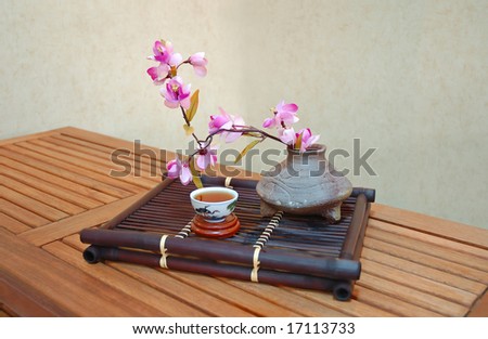 Cup of tea with pink orchids ikebana in handmade vase on black bamboo tea-tray