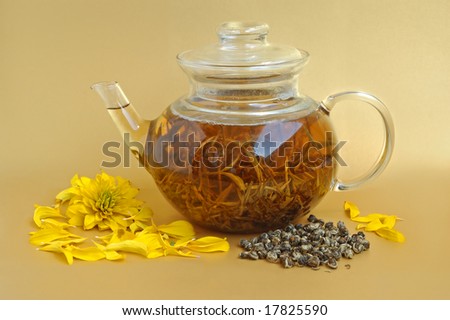 Glass teapot with dry tea leaves and flower on yellow background