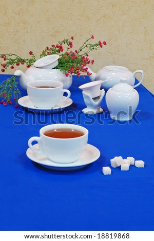 Cups of English tea with tea service and pink wild flowers on an blue table