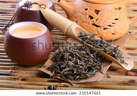 Teapot and aromatic oolong tea leaves on bamboo mat background