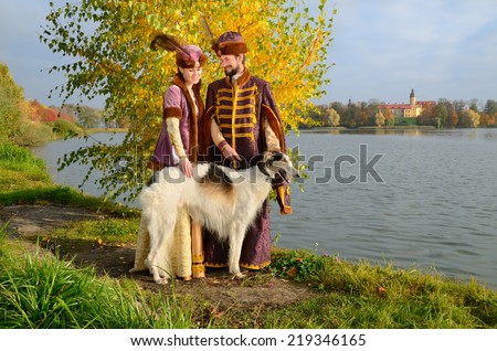 Nesvizh, Belarus - October 12: Couple in costumes of Grand Duchy of Lithuania with Russian borzoi dog represents everyday life of the nobility with Nesvizh Castle in background on October 12, 2013.