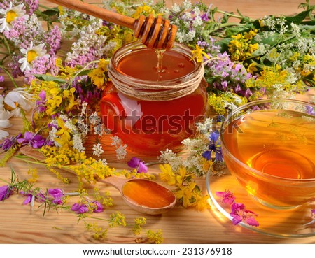 Tea in cup and gold honey in glass jar on wooden table with flowers