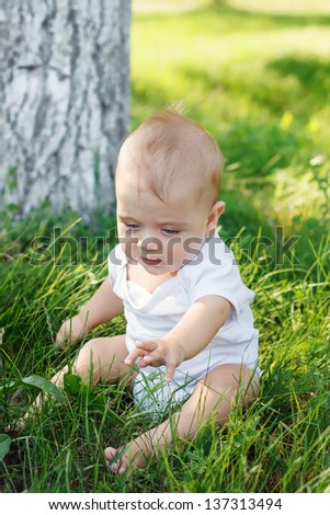 Little boy with a happy kind sits on a grass