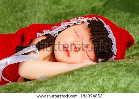 Two week old newborn baby girl dressed as Little Red Riding Hood and sleeping on a vintage wooden picnic basket surrounded with flowers.