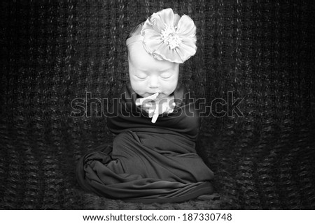 A sleeping two week old newborn baby girl wearing a vintage lace headband with flower.