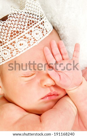 Newborn 12 day old baby boy lying on his back relaxing under a wrap cloth. Portrait old newborn baby boy wearing a gold crown.