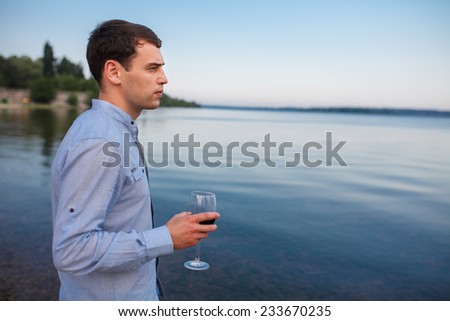 Young man with a bottle of wine and glasses on the beach at sunset