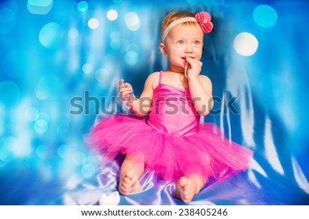 Cute happy blond baby girl in pink tutu and flower head band standing on blue background by smashed double tier heart decorated pink fondant iced cake with dirty sticky hands from messy crumb cake
