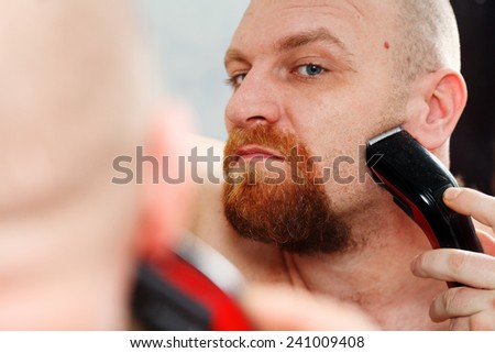 Making his beard perfect. Confident young bearded man shaving with electric razor
