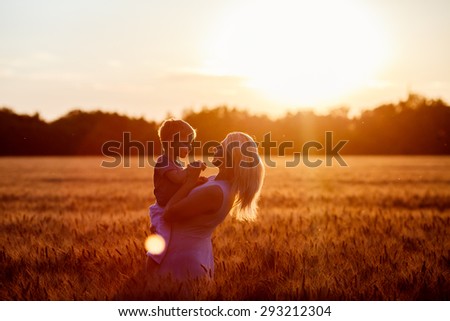 Happy family. Young mother throws up baby in the sky, on sunny day. Portrait mother and little son on  the  Field. Positive human emotions, feelings, emotions.Toned in warm colors