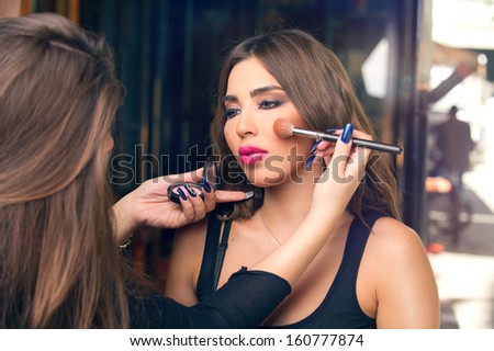 Professional makeup artist applying make up on a beautiful young model's face