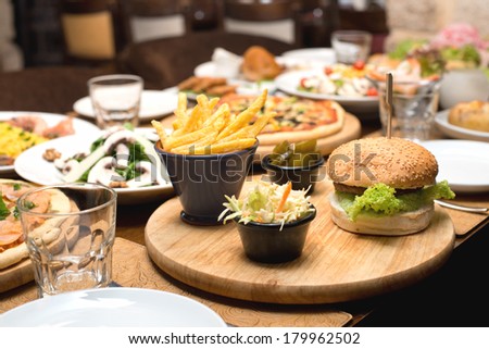 Beef burger and french fries on a table with other food plates in the background