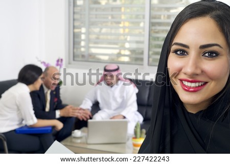 Arabian Businesswoman in office with Businesspeople meeting in the background, Arabian woman wearing Hijab in office with her colleagues in background