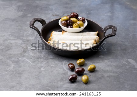 Plate of cheese sambusek,traditional Arabic food / Cheese rolls plate with olives served in a black pan on a rustic background