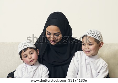 Arabian woman holding her children, mother and sons sitting on the couch in their living room