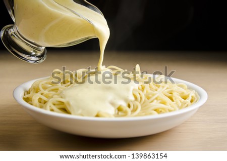 Pouring white sauce over plate of cooked spaghetti