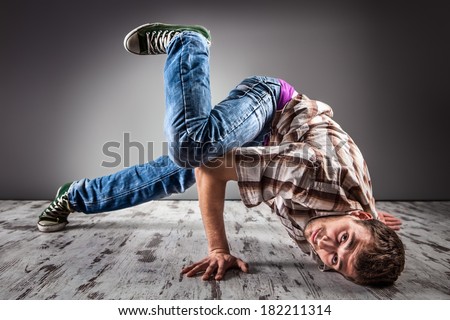 Young caucasian man performing break dance over a gray background/Modern hip-hop style teen breakdancing