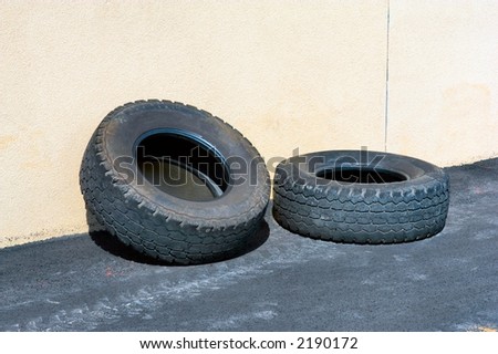 Two tire old tires leaning against a concrete wall