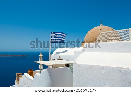 Oia Orthodox church and Greek flag on the edge of the Santorini caldera cliff on the island of Thira (Santorini), Greece.