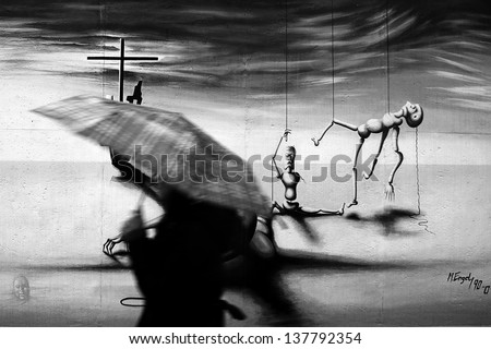 BERLIN, GERMANY - JANUARY 02: A woman with umbrella passes a image of the East side gallery on January 02, 2012 in Berlin. The wall is the longest open air gallery in the world