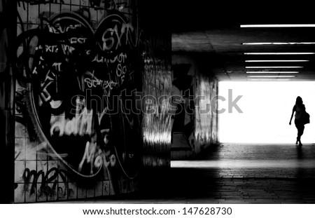 A Pedestrian Crosses A Dark, Tiled Tunnel With Graffiti On The Walls/In The Dark Tunnel
