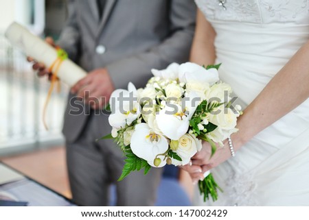 Wedding bouquet in the bride\'s hands, on background the groom with wedding contract