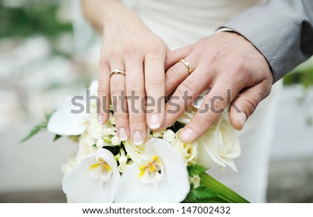 hands of the bride and the groom with wedding rings on wedding bouquet