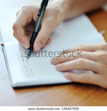 male student hand with a black pen writing on a white notebook
