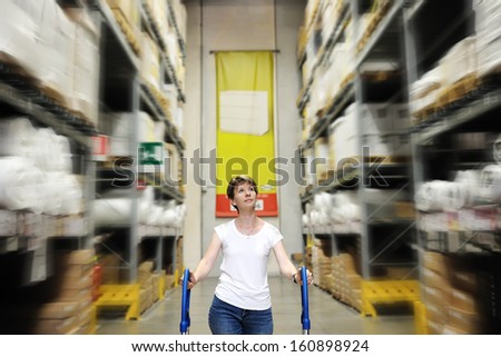 young woman walks pushing the cart between the high shelves of a home improvement store in a shopping mall