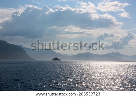 Seascape at the noon with island and mountains in the background