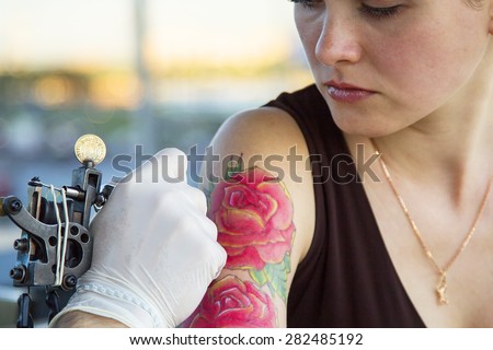 tattooer showing process of making a tattoo on young beautiful hipster woman with red curly hair hand. Tattoo design in the form of rose
