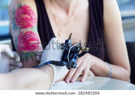 tattooer showing process of making a tattoo on young beautiful hipster woman with red curly hair hand. Tattoo design in the form of rose
