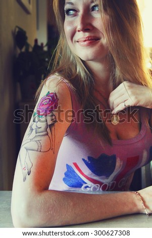 tattooer showing process of making a tattoo on young beautiful hipster woman with blonde hair hand. Tattoo design in the form pin-up girl with flower head. Vintage style picture