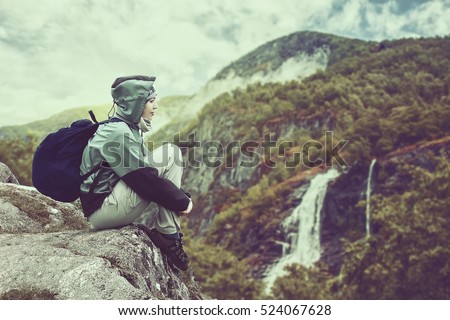 Woman traveler with backpack hiking in Norway mountains with magnificent waterfall. Beautiful autumn sunset landscape near Flam . Vintage style extreme travel background .