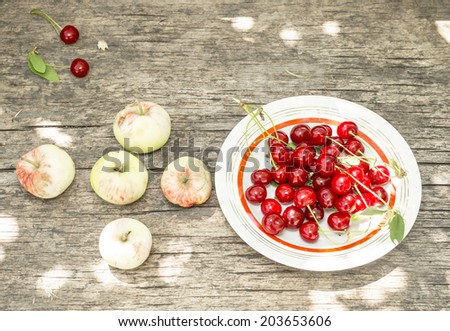 broken apples and a plate with cherries on old wooden table