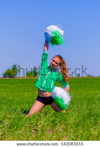 Cheerleader waves the pompons sitteing on the grass