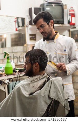 YAZD, IRAN - JANUARY 5, 2014: Unidentified Iranian haircutter cuts the beard of the client in Iran, Jan 5, 2014. Beard cutter is a popular profession in Iran
