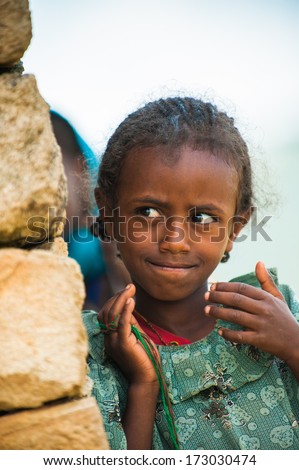 AKSUM, ETHIOPIA - SEP 24, 2011:Unidentified Ethiopian cute little girl in green dress near the stone wall in Ethiopia, Sep.24, 2011.Children in Ethiopia suffer of poverty due to the unstable situation