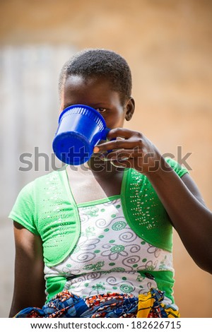 PORTO-NOVO, BENIN - MAR 9, 2012: Unidentified Beninese local beautiful woman drinks from a blue cup. People of Benin suffer of poverty due to the difficult economic situation.